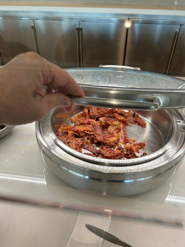a hand holding a tong over a silver pot with bacon