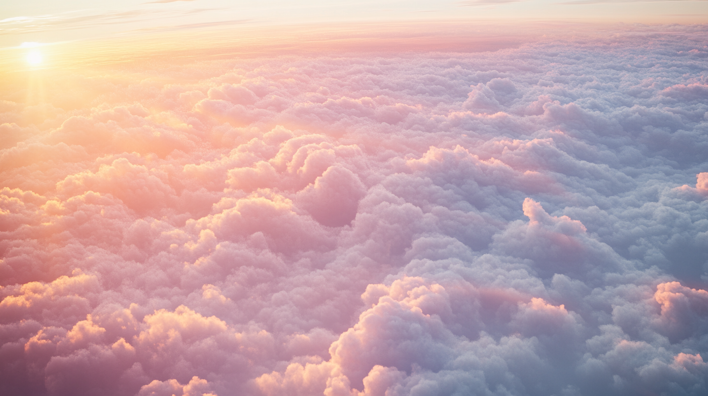 A beautiful view of fluffy clouds illuminated by a warm, golden sunrise. The clouds are tinged with soft pink and orange hues, creating a serene and dreamy atmosphere. The sun is partially visible on the horizon, casting gentle light across the sky.