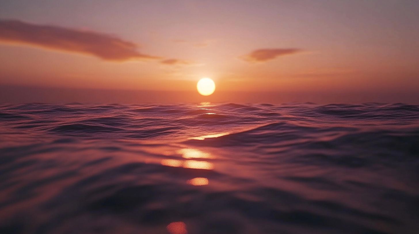 A serene ocean scene at sunset, with the sun low on the horizon casting a warm, golden glow over the gently rippling water. The sky is a gradient of soft pink and orange hues, with a few scattered clouds.