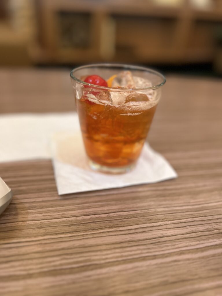 a glass of drink with ice and a cherry on a napkin