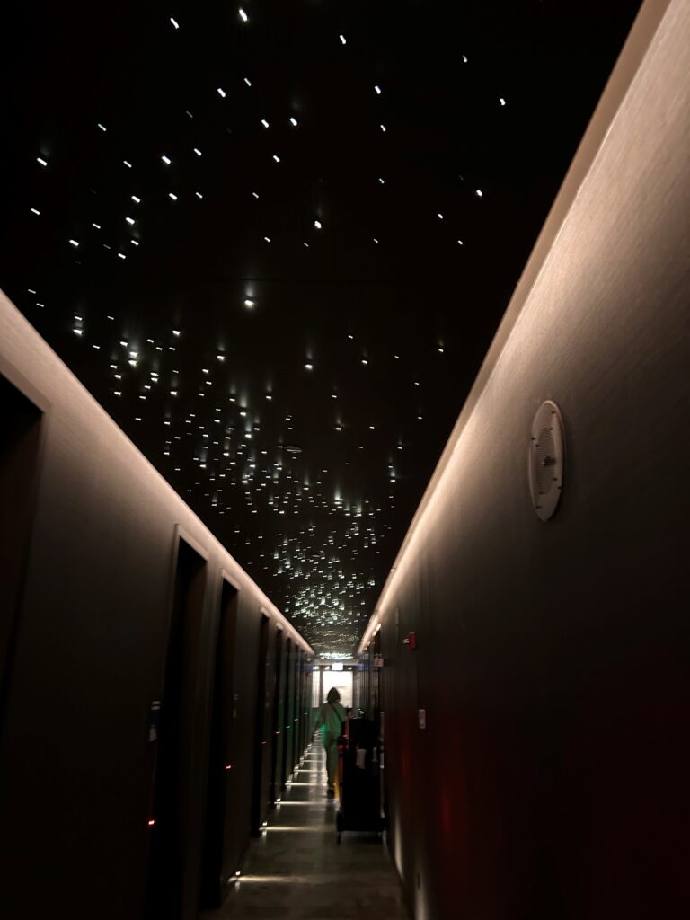 a person walking down a hallway with lights on the ceiling